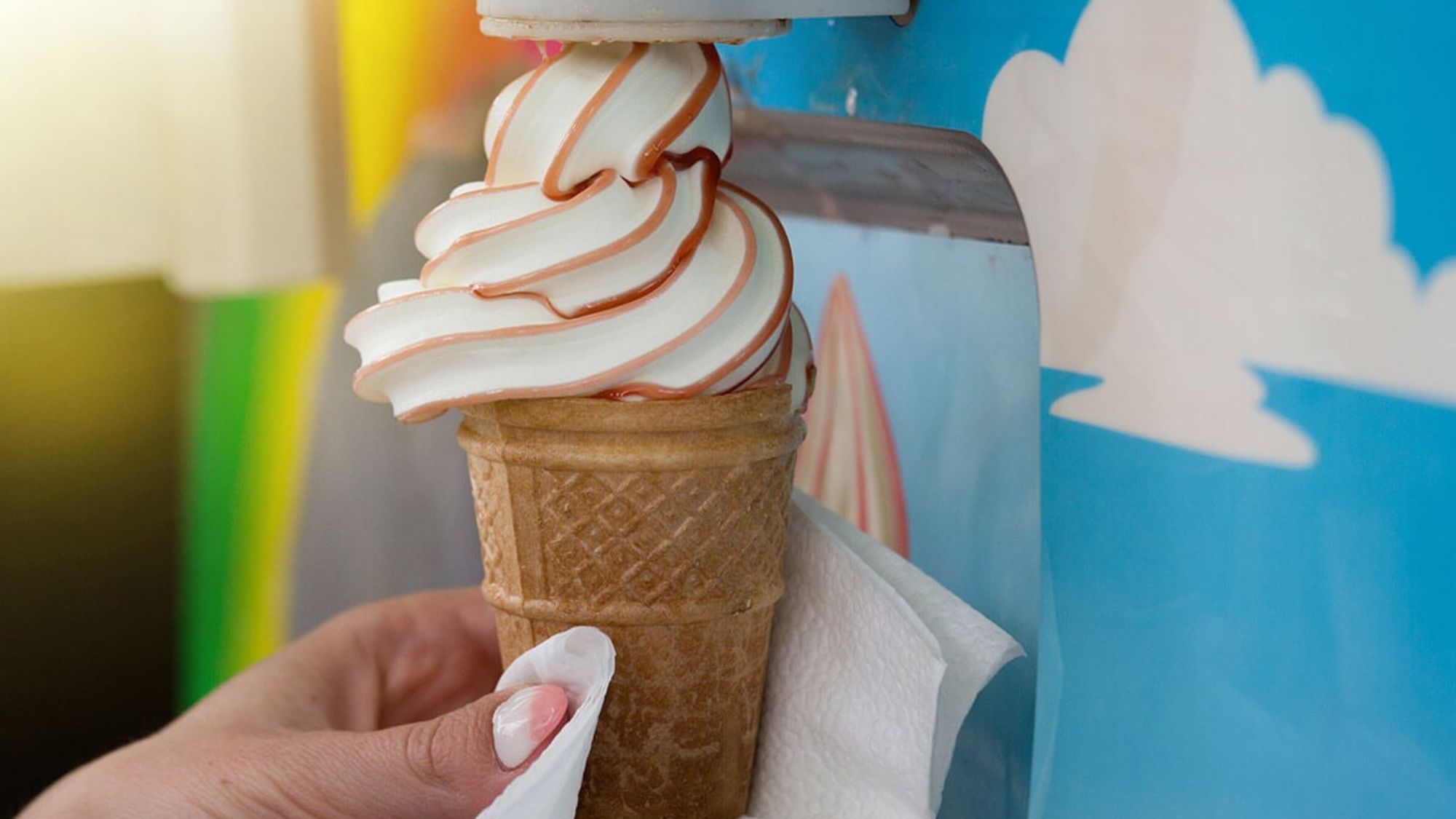 A person holds an ice cream cone with whipped cream, created using an ice cream machine
